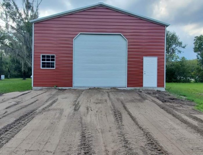 A red garage with a white door and dirt.